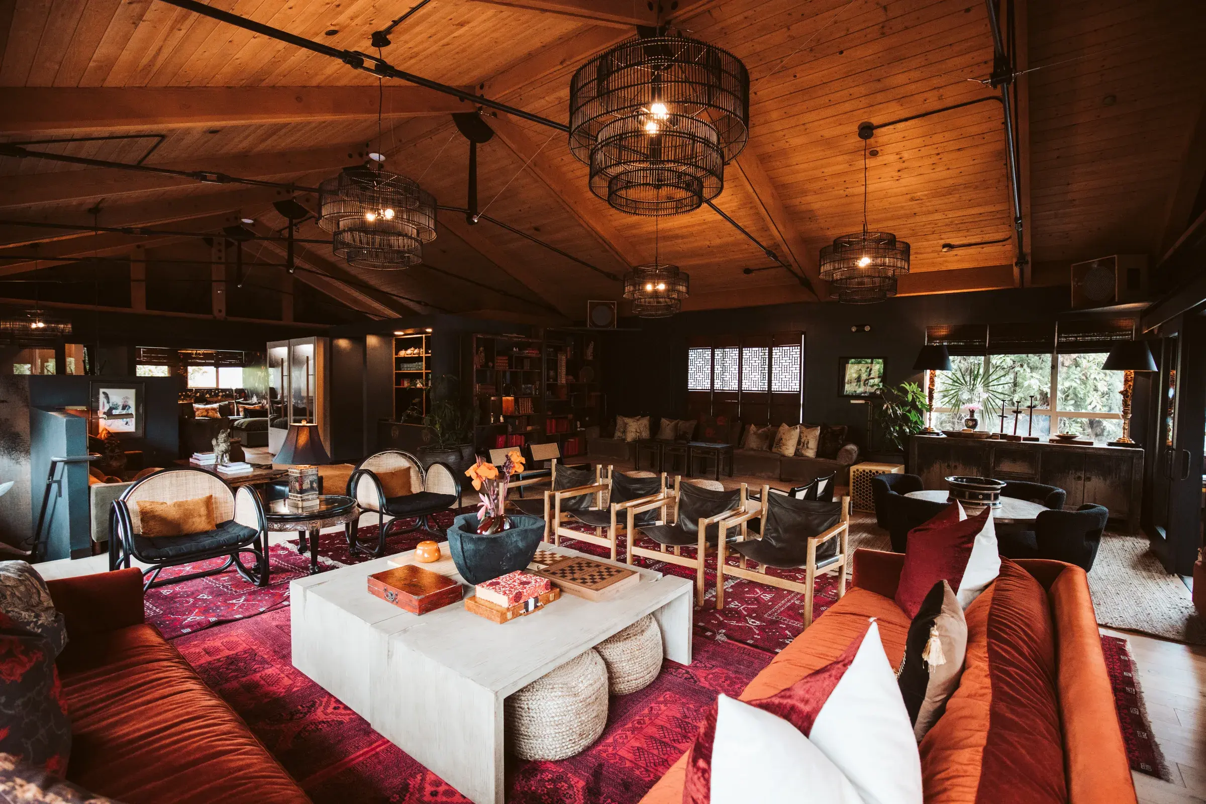 Wide view of clubhouse lounge with tiered cage chandeliers, leather sling chairs, bookshelves and layered red rugs