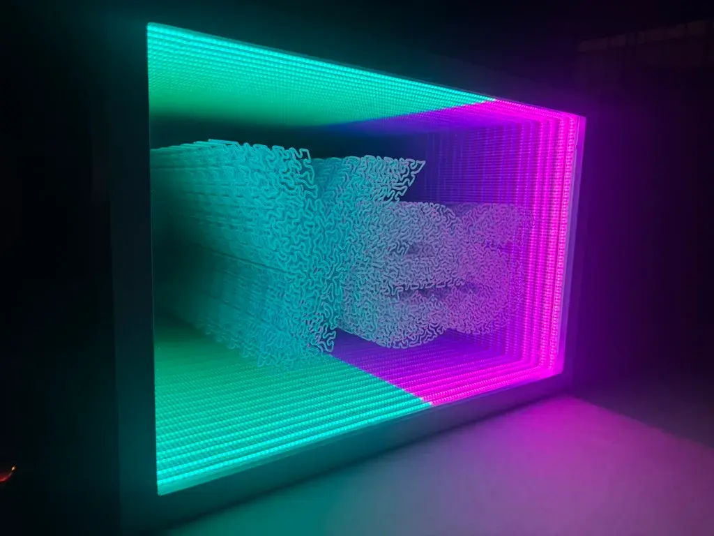 Infinity-mirror light box in a dark room, teal and magenta LED grid receding around sculpted script lettering
