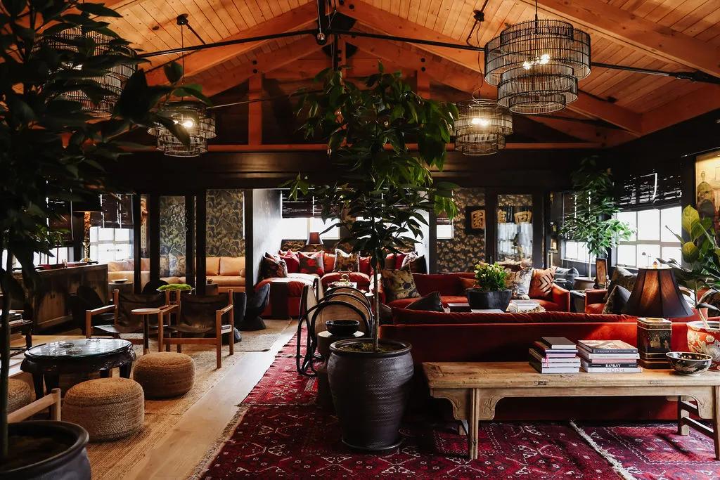 Vaulted timber hall with tiered cage chandeliers, mature indoor trees, rust velvet seating and layered red rugs