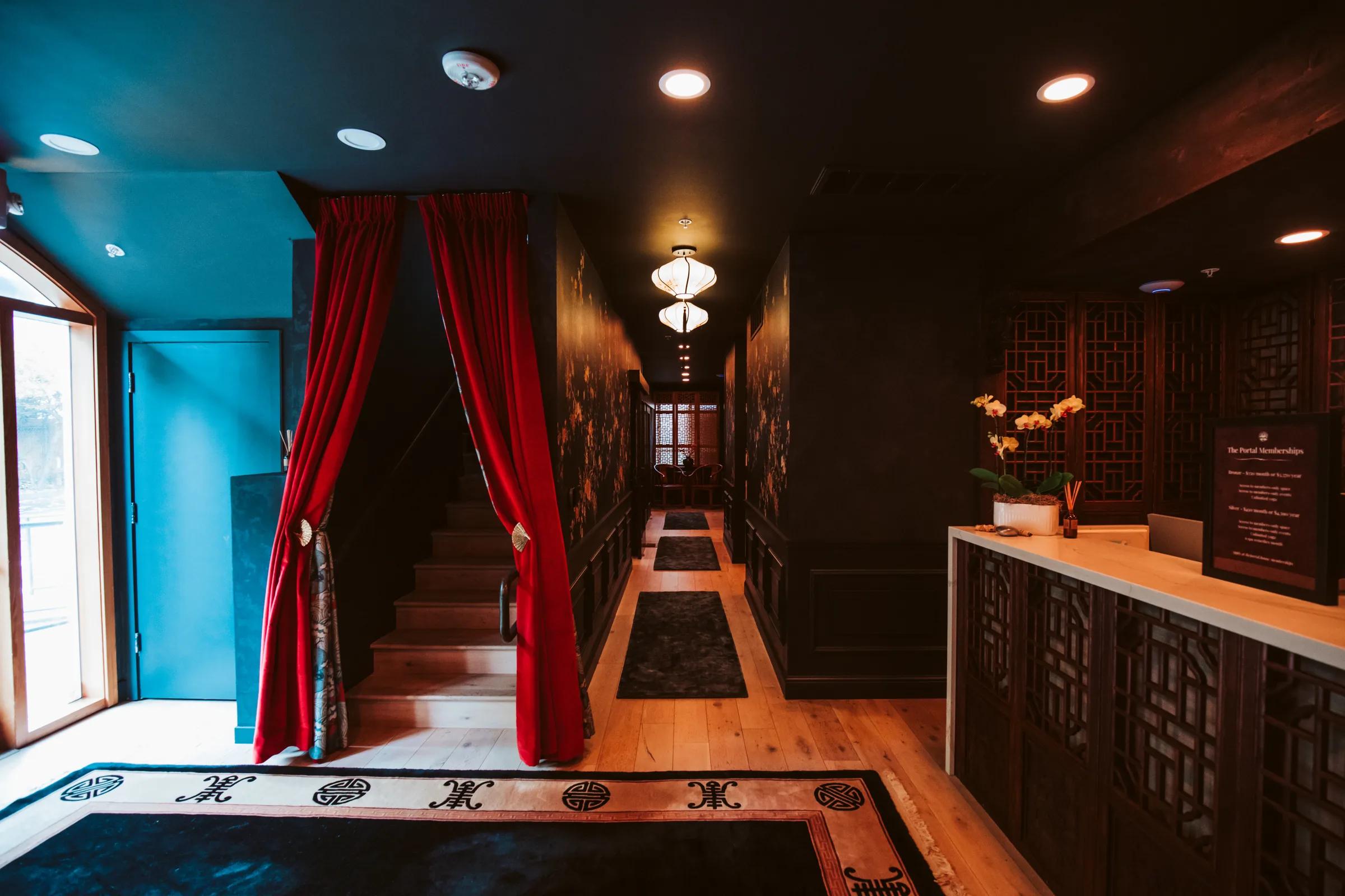 Entry hall with red velvet stair curtains, carved fretwork reception desk and a lantern-lit corridor