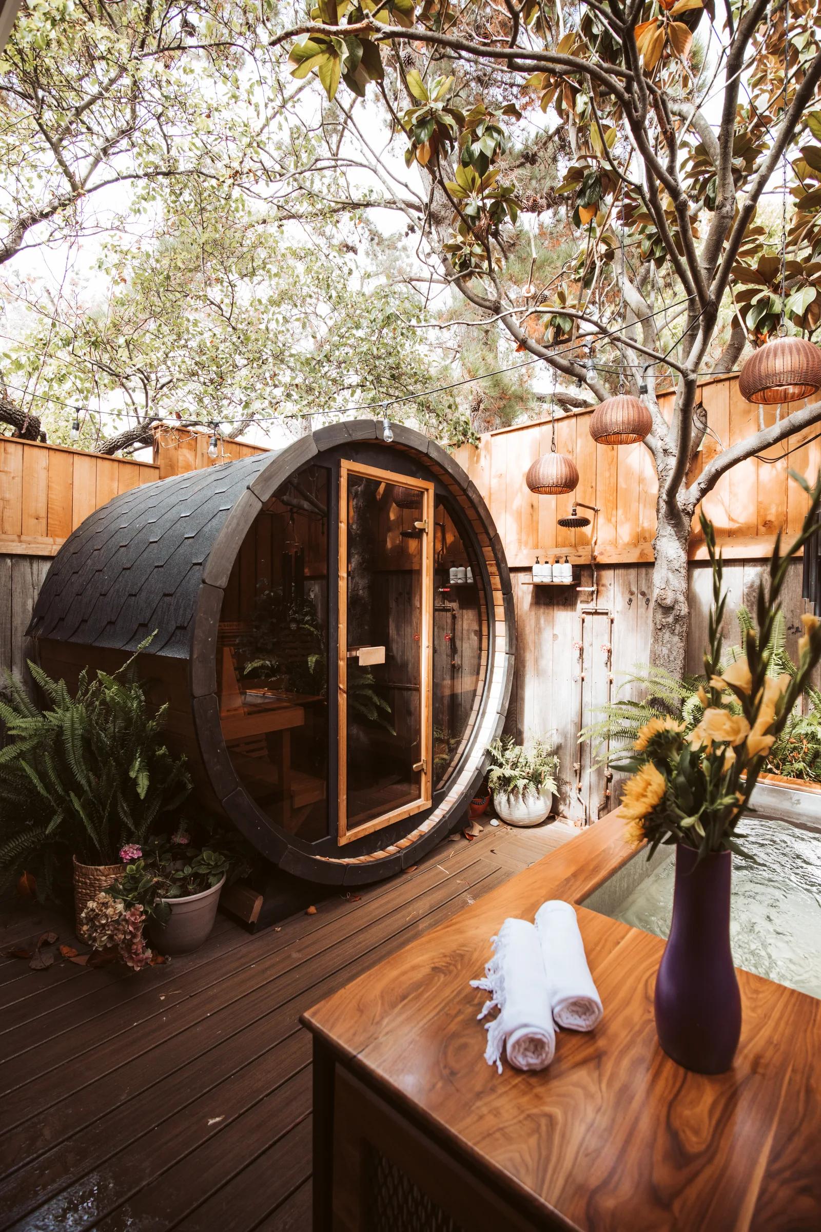 Backyard spa deck with barrel sauna, walnut cold plunge and hanging rattan lanterns under a magnolia tree
