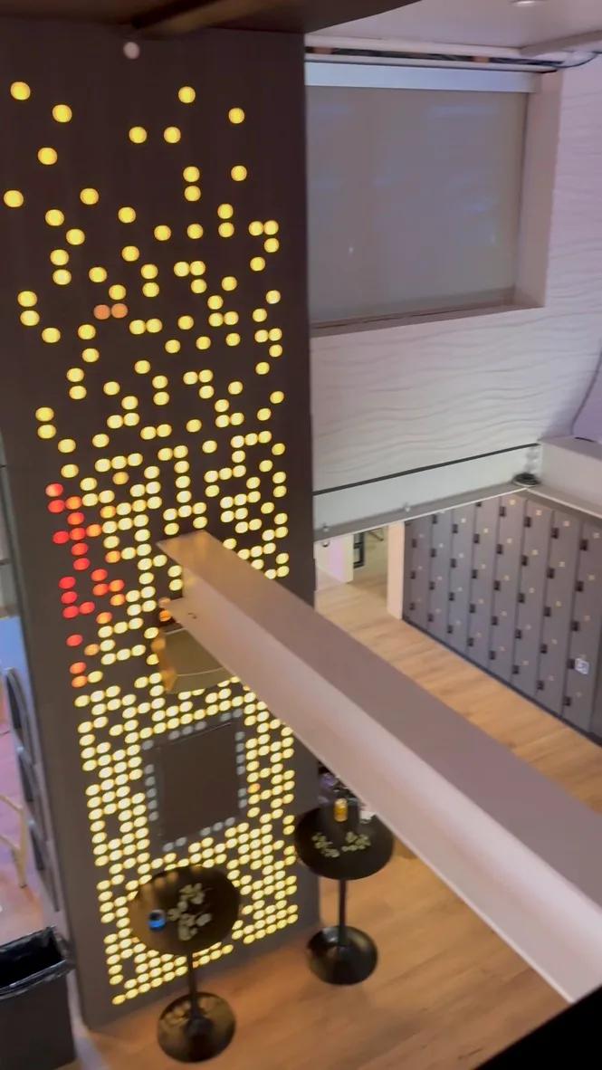 Two-story amber LED dot-matrix panel beside a staircase and bar tables, viewed from a mezzanine