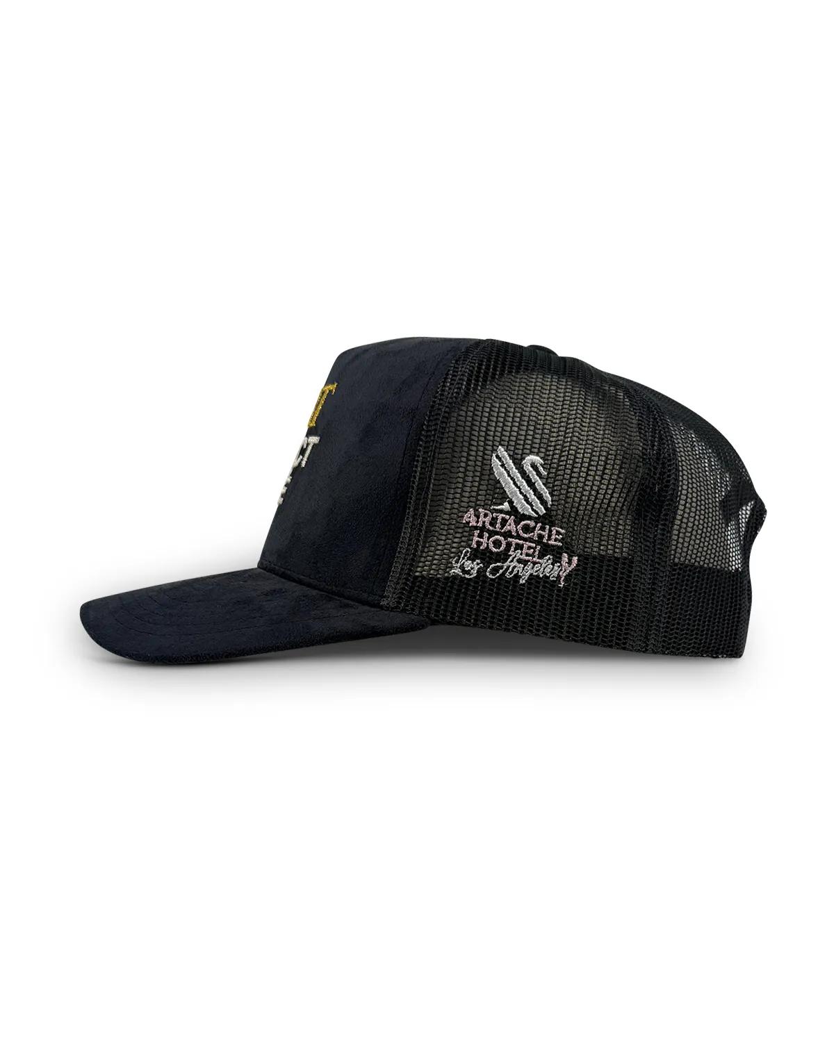 Suede trucker cap seen from the side, showing the black mesh back panel and an ArtAche Hotel Los Angeles script embroidered on the side
